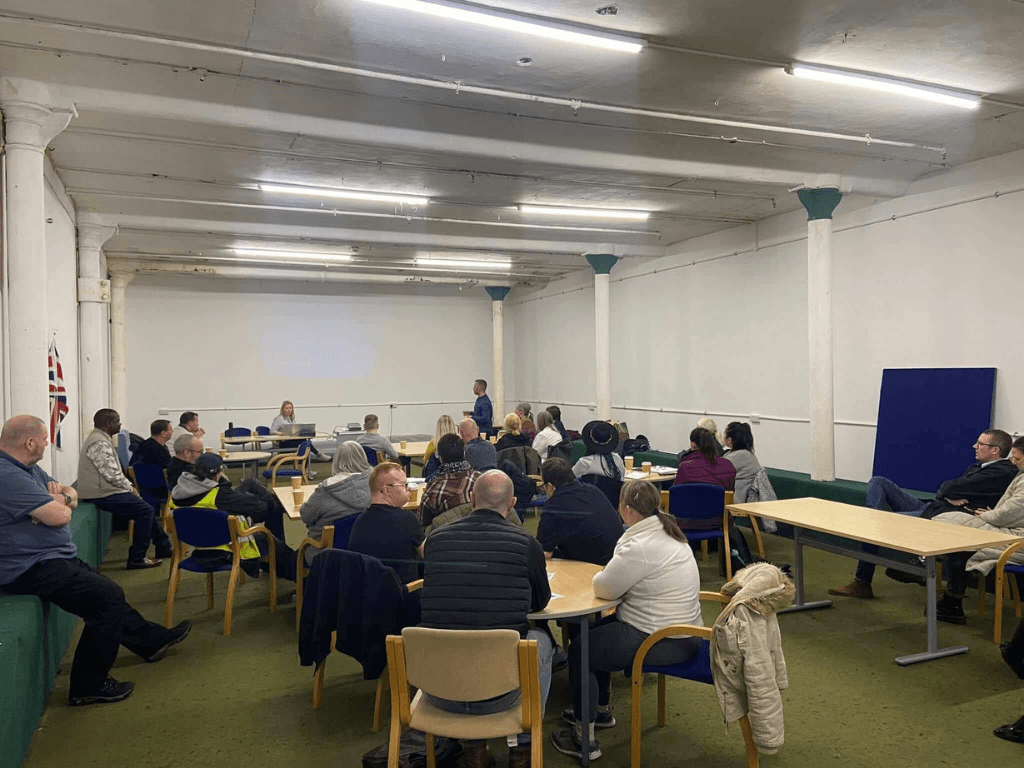 Community meeting taking place in the Community Room at Leigh Spinners Mill, with local residents gathered for a presentation and discussion.