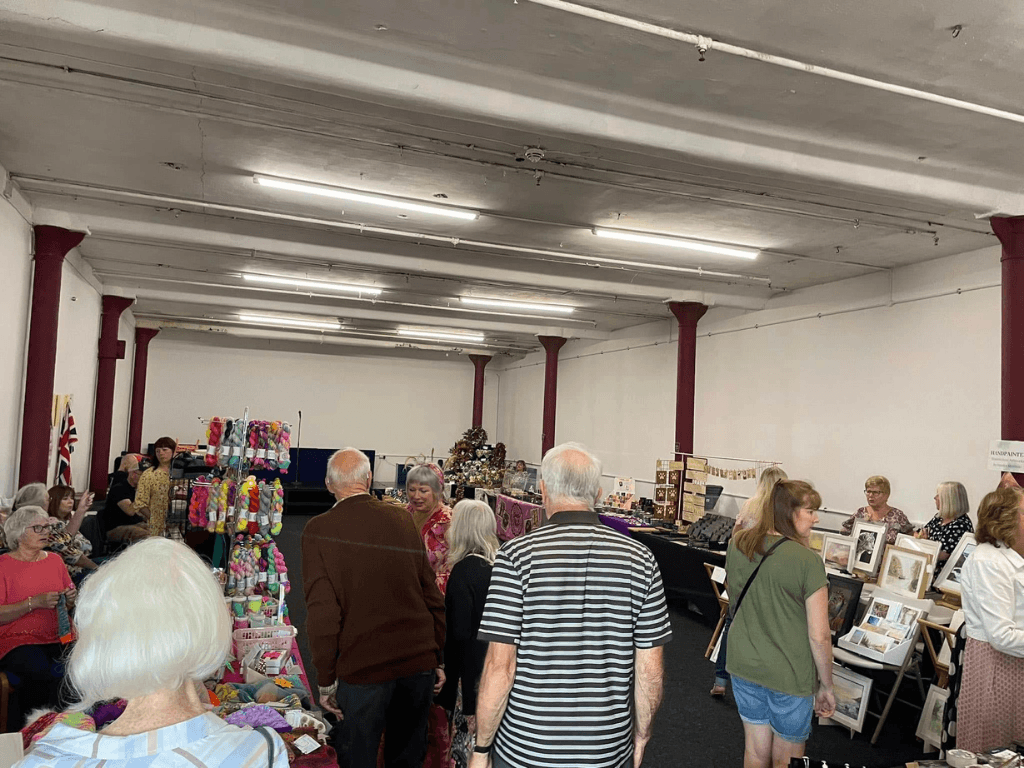 Community craft fair taking place in the Community Room at Leigh Spinners Mill, with local makers, stalls and visitors browsing handmade products and artwork.