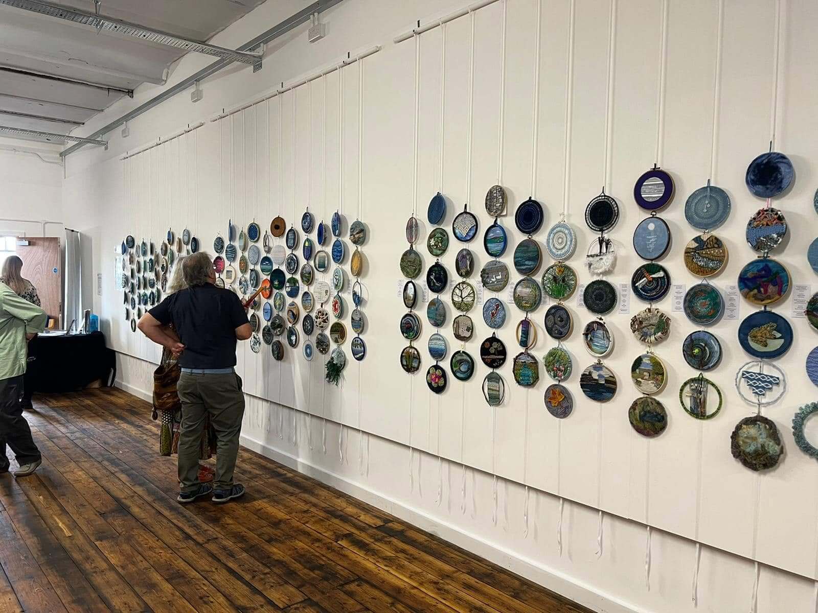 Visitors viewing a textile art exhibition in the Horrocks Gallery at Leigh Spinners Mill, featuring embroidered artworks displayed along the gallery wall.