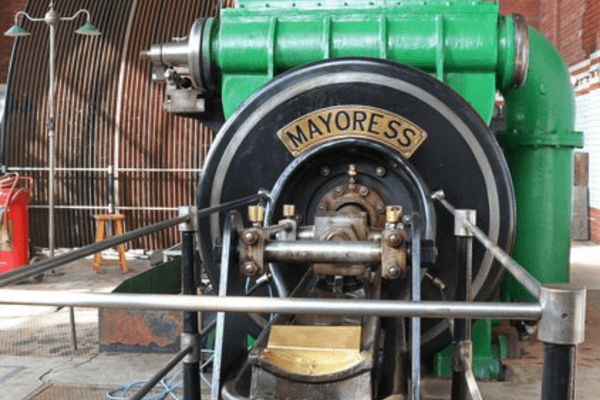 Front view of the restored Mayoress steam engine inside the engine house at Leigh Spinners Mill, highlighting its machinery and distinctive nameplate.
