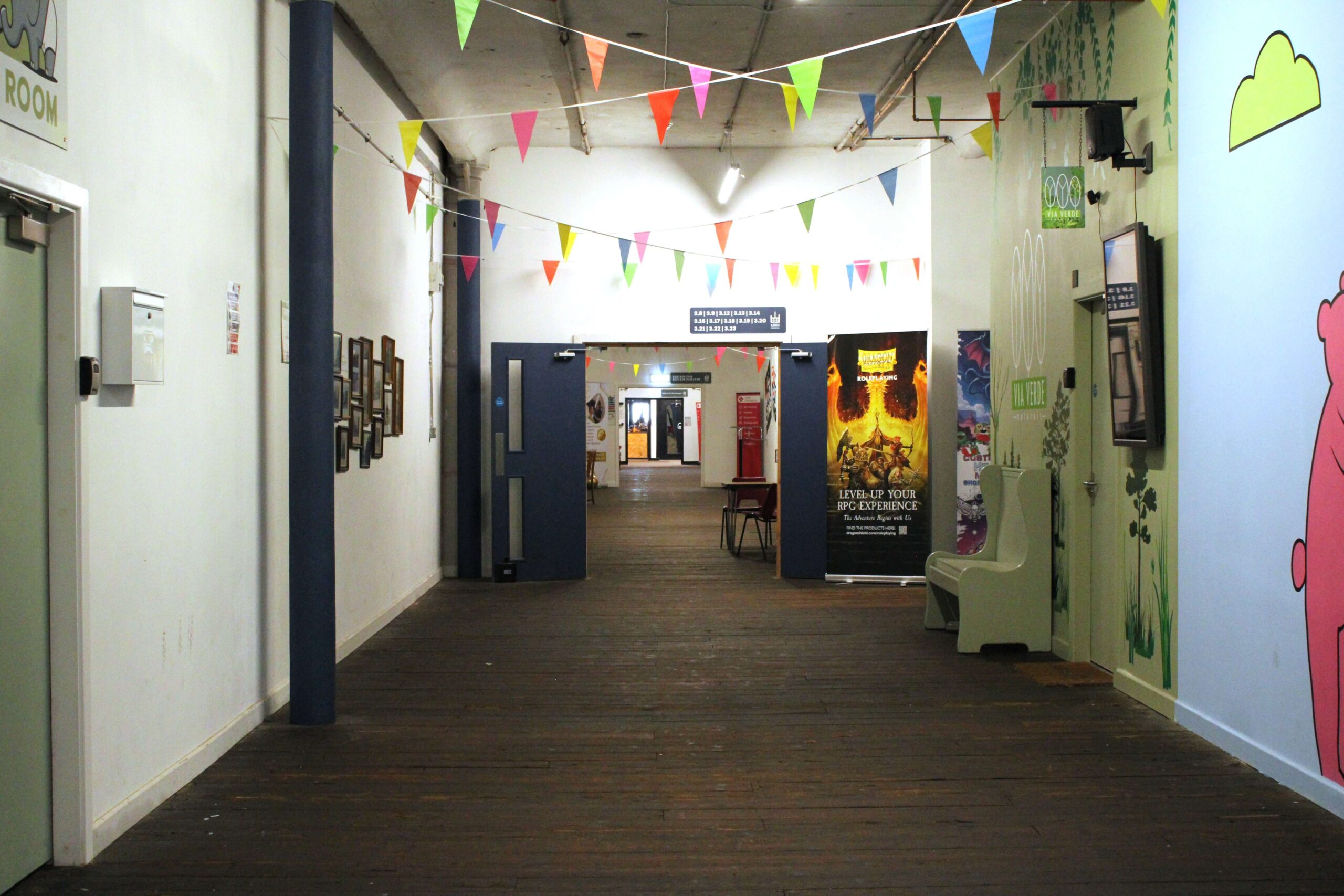 Interior walkway at Spinners Mill with colourful decorations, painted walls, historic wooden floors, and access to businesses and community facilities.