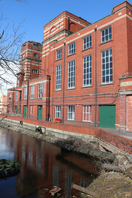 Historic view of Leigh Spinners Mill No. 2, featuring red brick mill buildings, tall windows and reflections in the mill lodge water.
