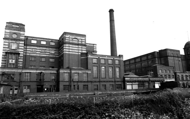 Black and white view of Leigh Spinners Mill featuring the red brick mill complex, chimney stack and industrial architecture before restoration.